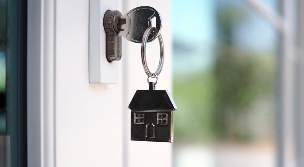 Image of key in the lock of a door. A key ring shaped like a house, hangs down. 
